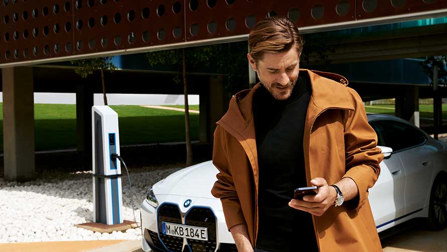 Meżczyzna używa telefonu podczas ładowania elektrycznego samochodu BMW